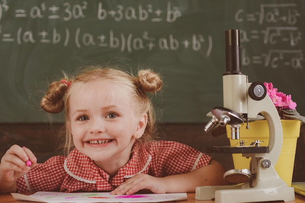 A criança faz trabalhos acadêmicos e de pesquisa em sala de aula. pesquisa de menina com microscópio no laboratório da escola, filtro vintage.