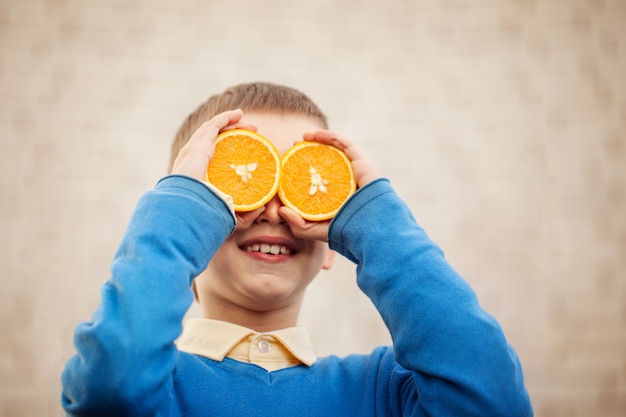 A criança feliz do retrato que guarda a laranja antes de seus olhos gosta no dia ensolarado.