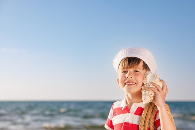 Foto a criança feliz escuta a concha na praia