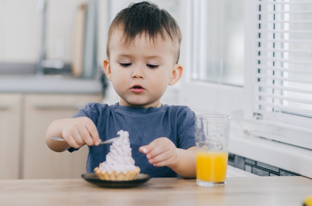 A criança na cozinha comendo um bolo com creme é muito apetitoso, colher