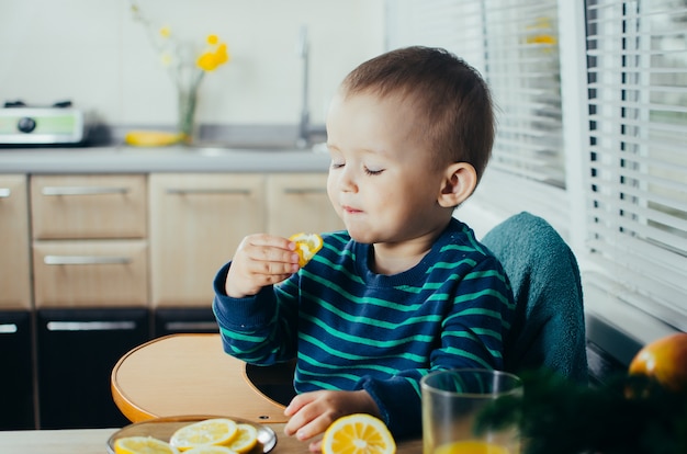A criança na cozinha comendo um limão delicioso e suculento, vida saudável