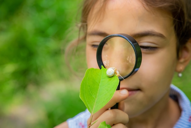 Foto a criança olha o caracol através de uma lupa. foco seletivo. natureza.