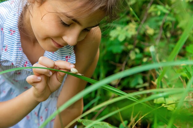 A criança olha o caracol através de uma lupa. Foco seletivo. Natureza.