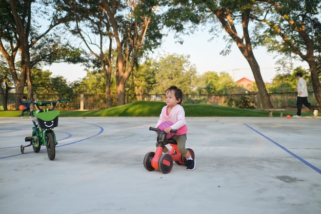 A criança pequena adorável aprendendo a andar de bicicleta no primeiro equilíbrio. Crianças andando de bicicleta no parque