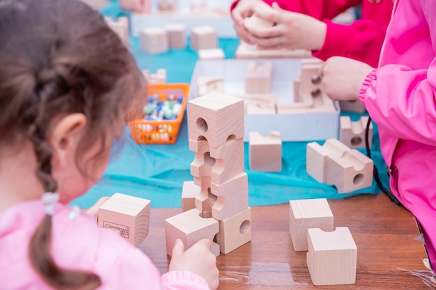 A criança pequena brinca com uma criança pré-escolar construtora de madeira aprendendo em casa para fazer mosaico Desenvolvimento inicial Brincando e aprendendo As mãos das crianças coletam o conceito de atividade de cubos construtores