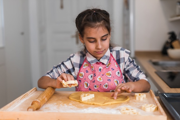 Foto a criança prepara biscoitos e recorta estatuetas de massa enrolada em forma de coração. mãos de criança fazendo biscoitos de massa crua em forma de coração, close-up.