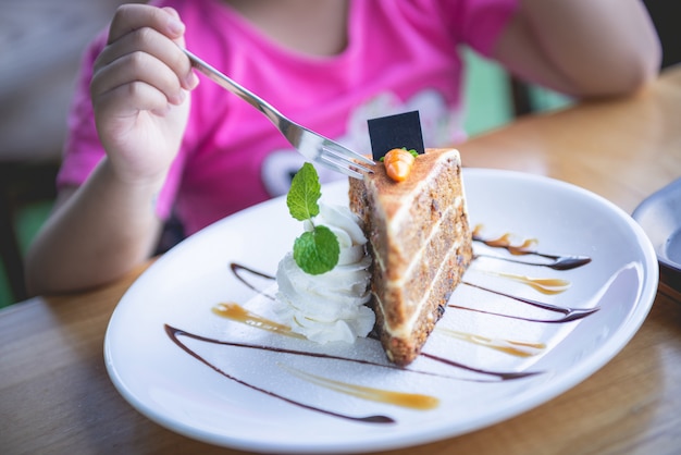 A criança que come o bolo de cenoura decorou com chantiliy, caramelo, folhas de hortelã na cor branca da placa.