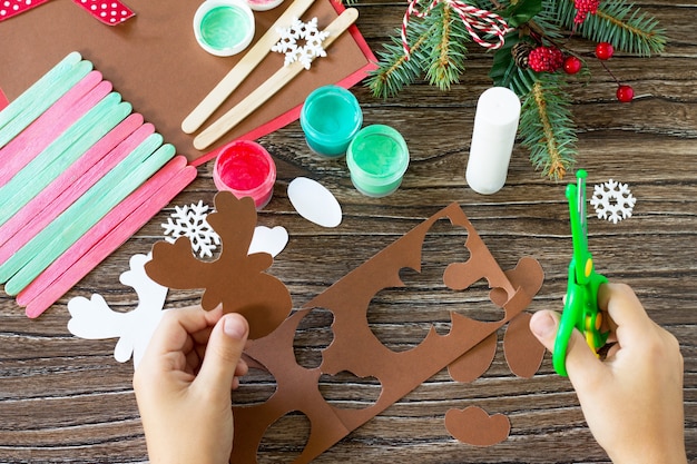 Foto a criança recorta os detalhes para presente de pau de papai noel e renas feito à mão