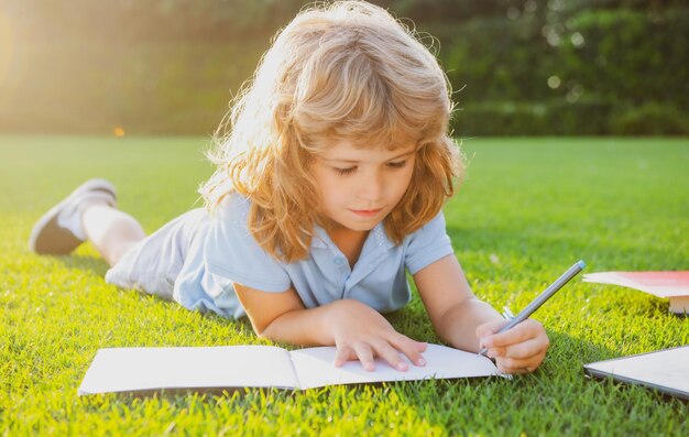 A criança relaxa no garoto de férias com lápis escrevendo no caderno no fundo da grama