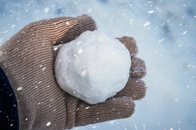 A criança segura uma bola de neve nas mãos durante uma nevasca