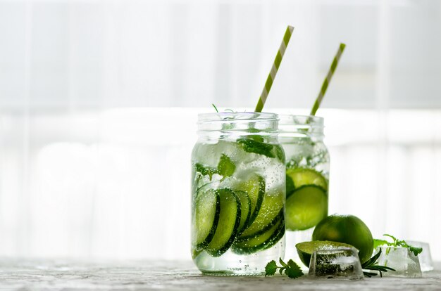 A desintoxicação fria e refrescando molha com cal, pepino, alecrins e gelo no frasco de vidro. Copyspace