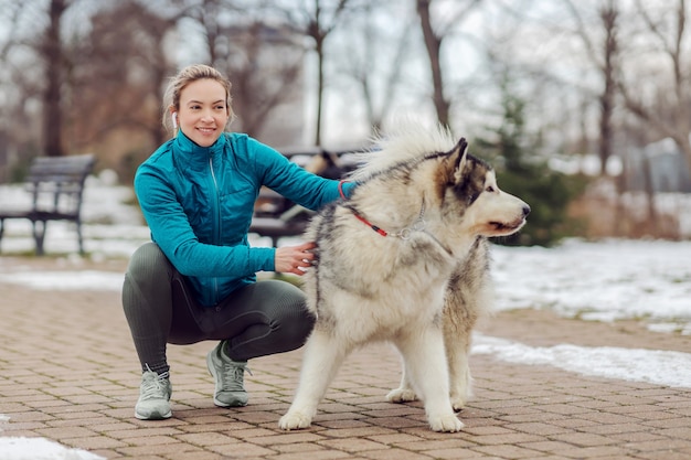 A desportista em forma foi passear com o cão na neve. Parque da cidade, neve, fitness de inverno, animais de estimação