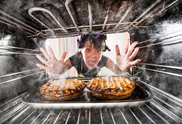 Foto a dona de casa engraçada negligenciou os bolos no forno, então ela se queimou, vista de dentro do forno. dona de casa perplexa e com raiva. perdedor é o destino!