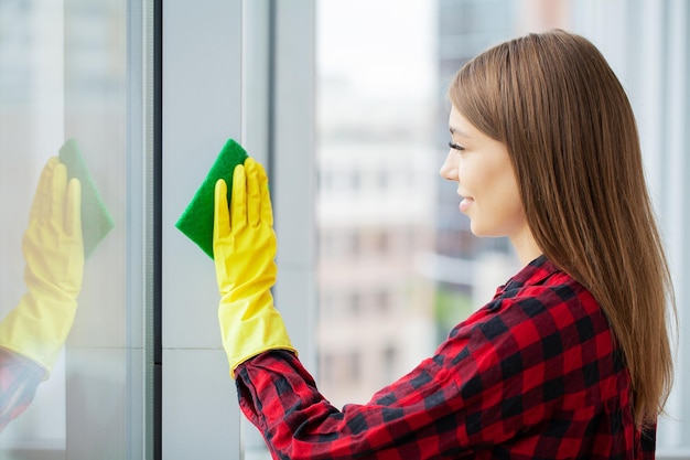 A dona de casa feliz da jovem mulher lava uma janela
