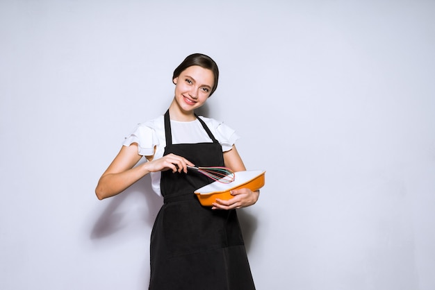 A dona de casa jovem feliz com avental preto prepara comida deliciosa, bolo