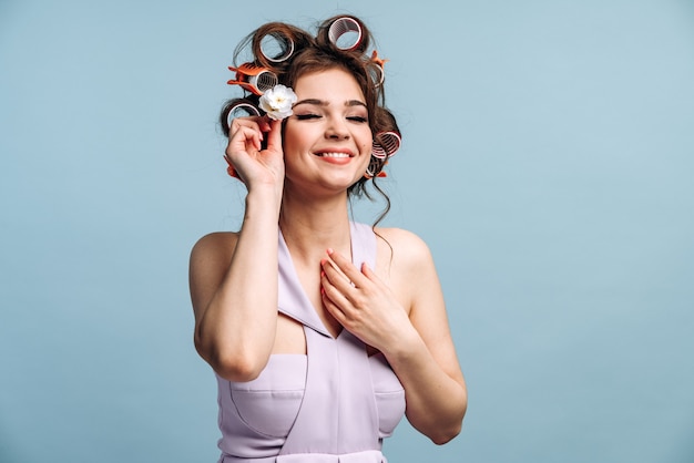 A dona de casa morena sorridente com rolos e um lindo vestido enfia uma flor branca no cabelo.