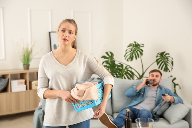 A dona de casa triste com roupa suja e o marido preguiçoso descansando no sofá