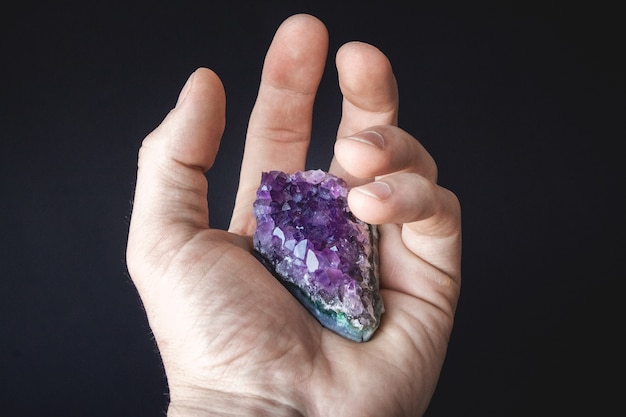 A drusa de cristais violetas naturais não tratados de ametista em um pedaço de rocha está na palma da sua mão.