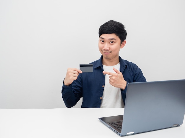 A emoção feliz do homem senta-se com o laptop na mesa aponte o dedo no cartão de crédito à disposição