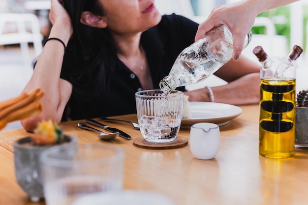 A empregada de mesa a derramar água em copos de garrafa na mesa.