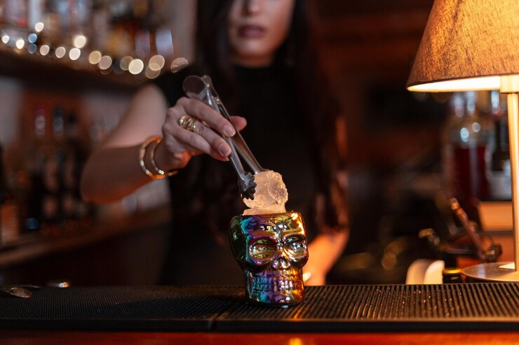 Foto a empregada do bar faz um coquetel alcoólico e coloca um cubo de gelo num crânio de vidro no balcão do bar.