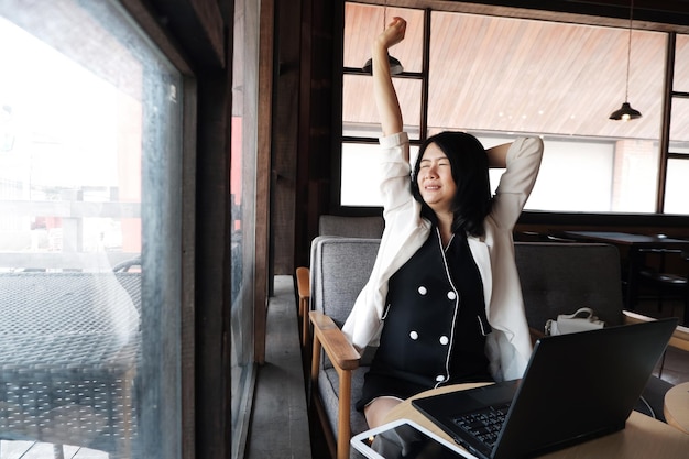 A empresária asiática sorridente se estica preguiçosamente no local de trabalho no escritório ou relaxa no café