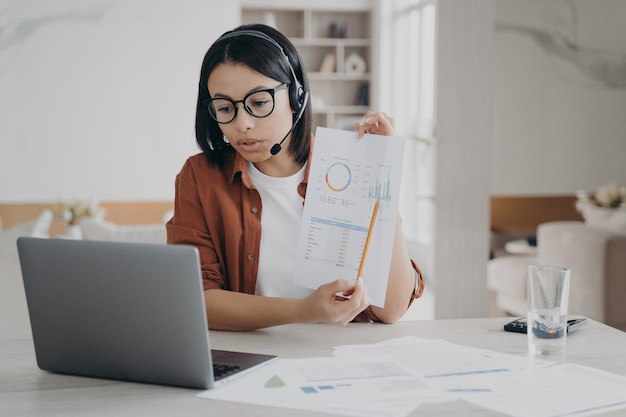 A empresária no fone de ouvido explica o cliente de consultoria de gráficos que faz a videoconferência funcionar no laptop