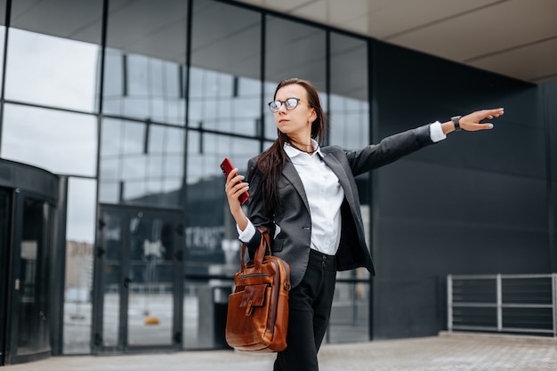 A empresária pega um táxi. Uma mulher está esperando um carro e irá a uma reunião de negócios. Conceito de negócios. Menina com óculos na cidade perto do trabalho.