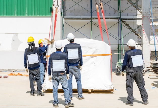 A engenharia com capacetes de segurança prepara uma máquina antes do guindaste industrial