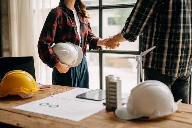 A equipe de construção aperta as mãos cumprimentando o início de um novo plano de projeto atrás do capacete amarelo na mesa no centro do escritório para consultas sobre o projeto de construção