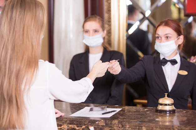 A equipe do hotel atende os hóspedes com máscaras médicas