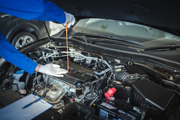 A equipe do mecânico de automóveis está puxando o medidor de nível de óleo para cima para verificar o nível de óleo. Para verificar a condição do carro