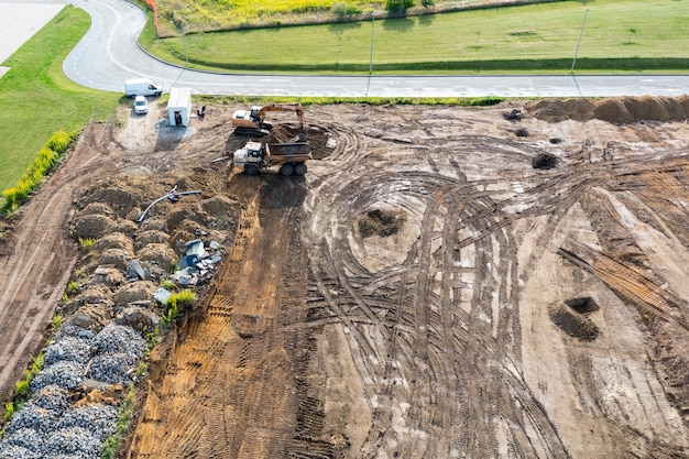 A escavadeira cava uma trincheira sob a fundação e a escavadeira limpa o terreno. Vista superior de um canteiro de obras