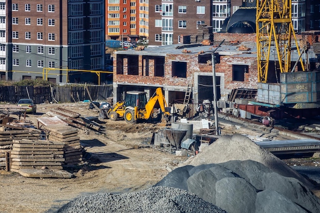 A escavadeira se move e espalha o solo e os escombros no aterro da estrada Trabalho em andamento em um novo bloco de apartamentos Canteiro de obras do novo edifício