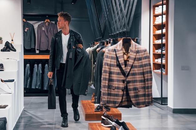 A escolha fez um jovem na loja moderna com roupas novas Elegante desgaste caro para homens
