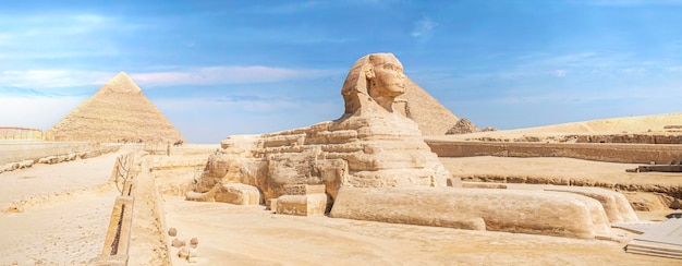 A escultura icônica da Esfinge adjacente às Grandes Pirâmides de Gizé, Egito A grande esfinge antiga em uma vista lateral de fundo azul