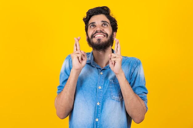 À espera de um momento especial retrato de jovem de camisa mantendo os dedos cruzados sobre fundo amarelo