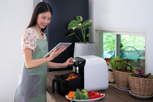 A esposa asiática fez a máquina de Oilless Air Fryer para cozinhar um frango frito para o jantar de hoje, esta imagem pode ser usada para alimentos, cozinha e conceito de tecnologia.