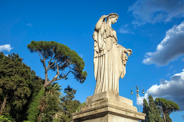 A estátua de uma mulher com um vestido longo e esvoaçante fica em frente a um céu azul.