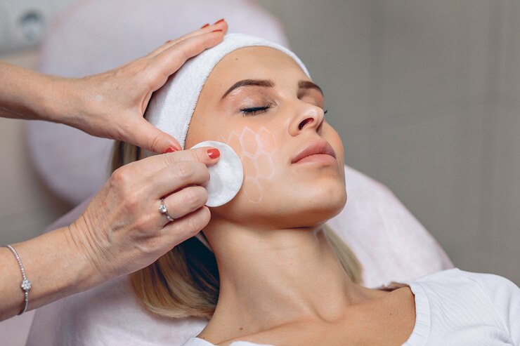 A esteticista mestre profissional apaga com uma almofada de algodão uma grade desenhada com um marcador branco no rosto de uma garota cliente.
