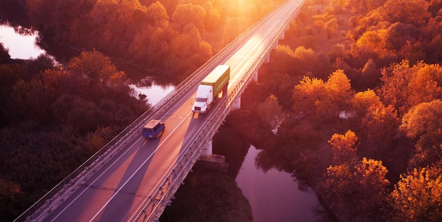 A estrada, a ponte sobre o rio em que os carros se movem. Amanhecer sobre a floresta de outono. Maravilhosa paisagem.