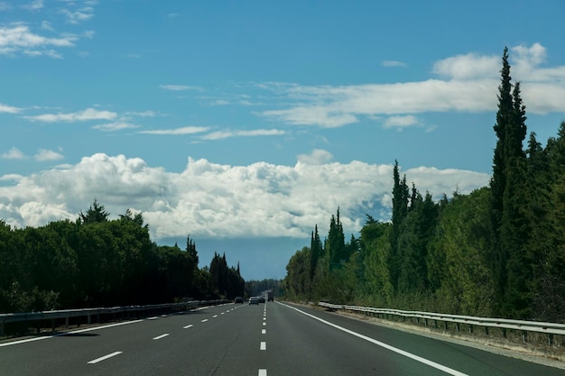 A estrada na Grécia é cercada por árvores verdes, céu azul e nuvens cumulus à frente