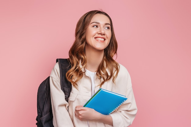 A estudante ri e sorri e desviando o olhar, mantendo um telefone móvel isolado em uma parede rosa. Garota freelancer feliz