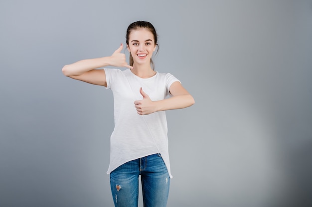 A exibição moreno de sorriso da mulher chama-me gesto imitando o telefone com a mão e os polegares isolados acima sobre o cinza