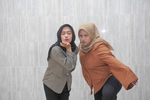A expressão feliz de duas mulheres indonésias asiáticas usando hijabs vestindo roupas castanhas e cinzentas
