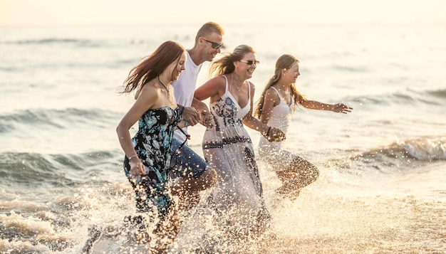 A família completa corre de mãos dadas da praia ao mar desfrutando de umas férias conjuntas à beira-mar