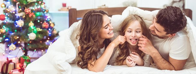 A família feliz deitada e se divertindo na cama perto da árvore de natal