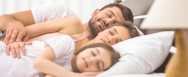 A família feliz dormindo na cama confortável