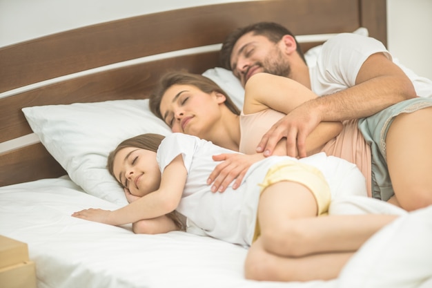 A família feliz dormindo na cama confortável