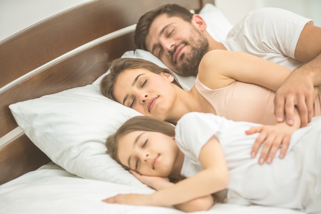 A família feliz dormindo na cama confortável
